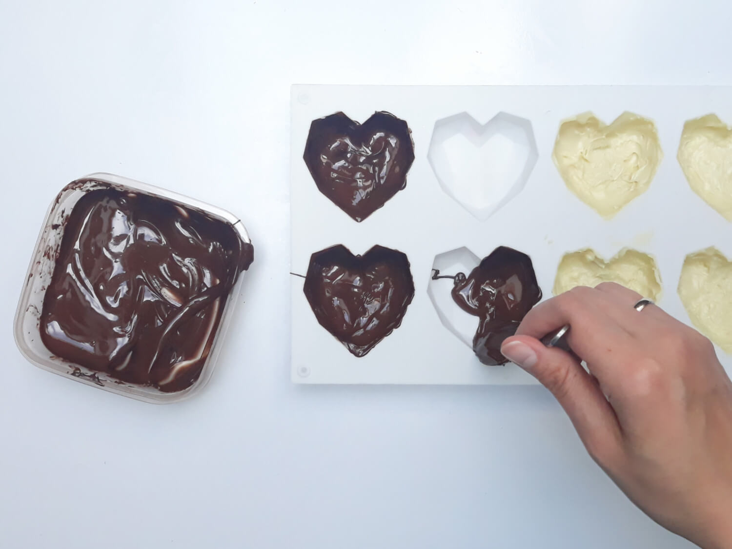 przygotowanie monoporcji w temperowanej czekoladzie, wypełnianie temperowaną białą czekoladą formy silikonowej w kształcie geometrycznych serc